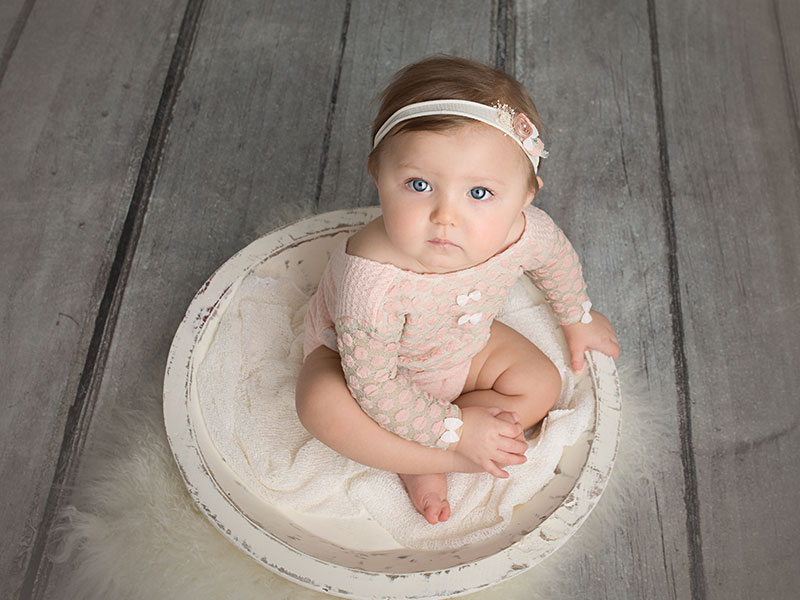 6 to 12 month old girl sitting in a bowl with a headband with a pink peach sitter session outfit on