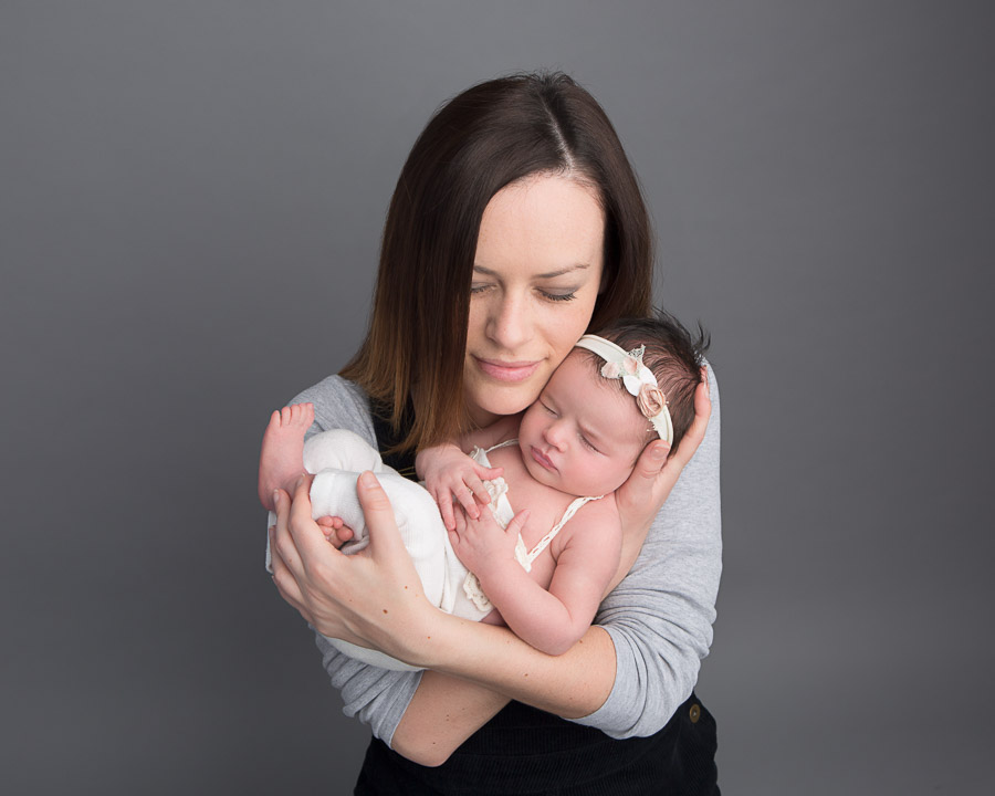 mum holding a 10 day old newborn baby girl in her arms cuddled under her chin in a photography studio