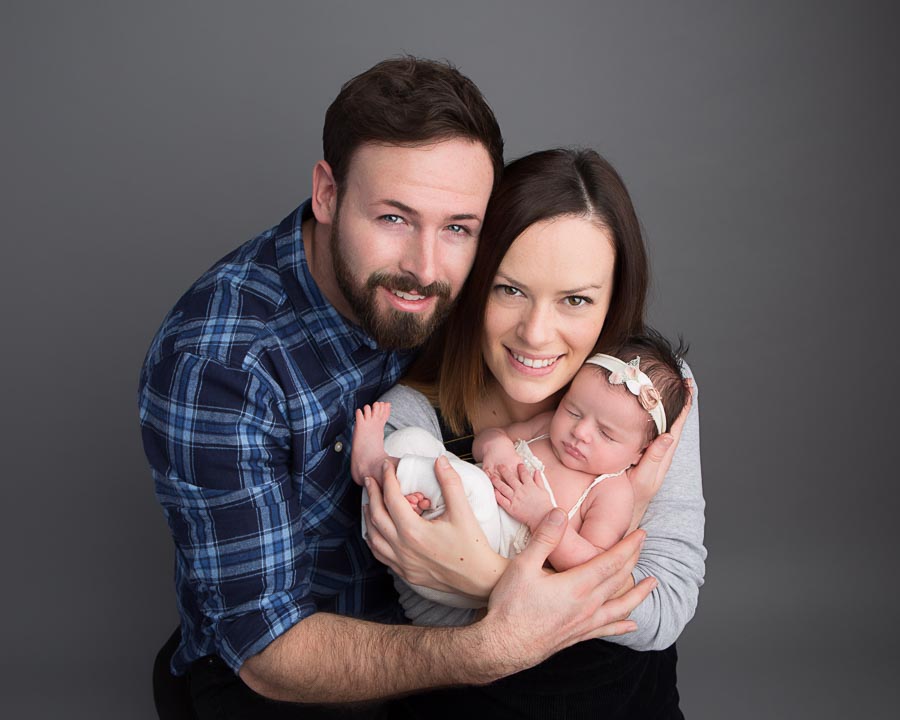 mum holding a 10 day old newborn baby girl with dad's arms around both of them in a photography studio.