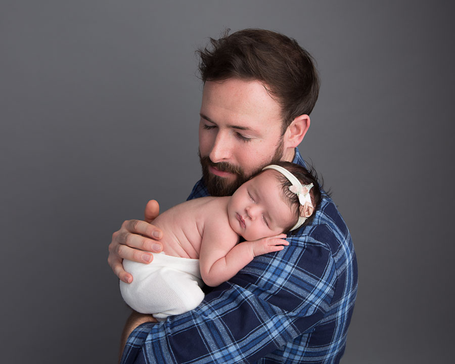 Dad holding his 10 day old newborn baby girl on his shoulder with his hand on her back cuddled in a photography studio