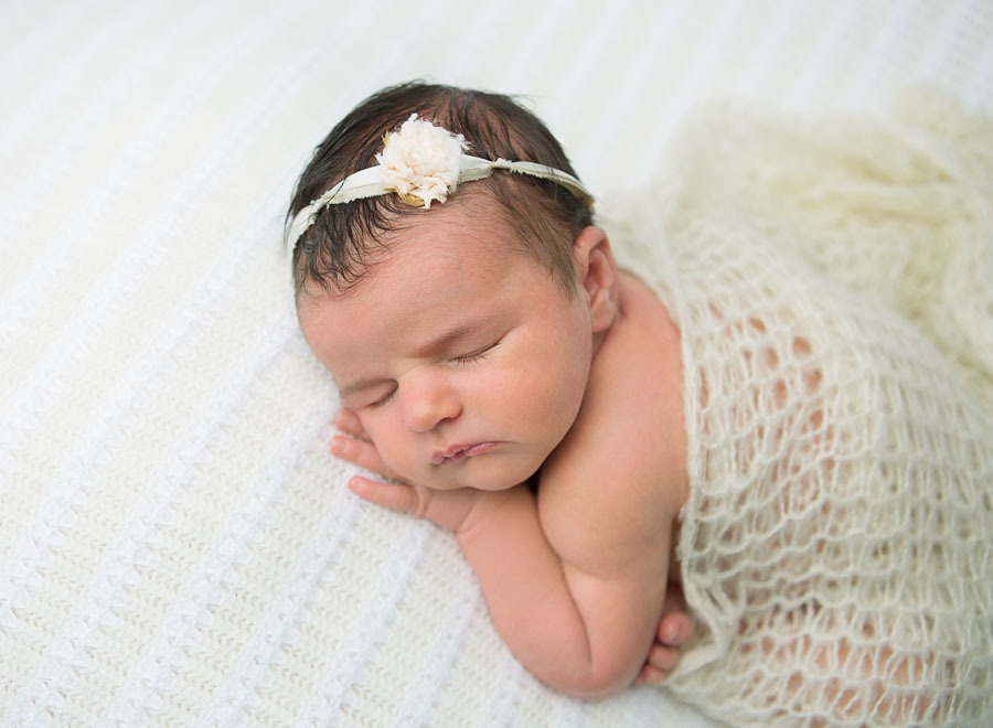 10 day old newborn baby girl posed in cream pants and cream headband posed on a cream backdrop in a photography studio
