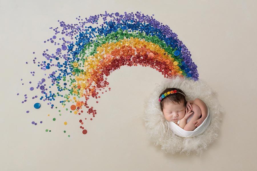 10 day old newborn baby girl in a white wrap and a rainbow headband on a digital rainbow background