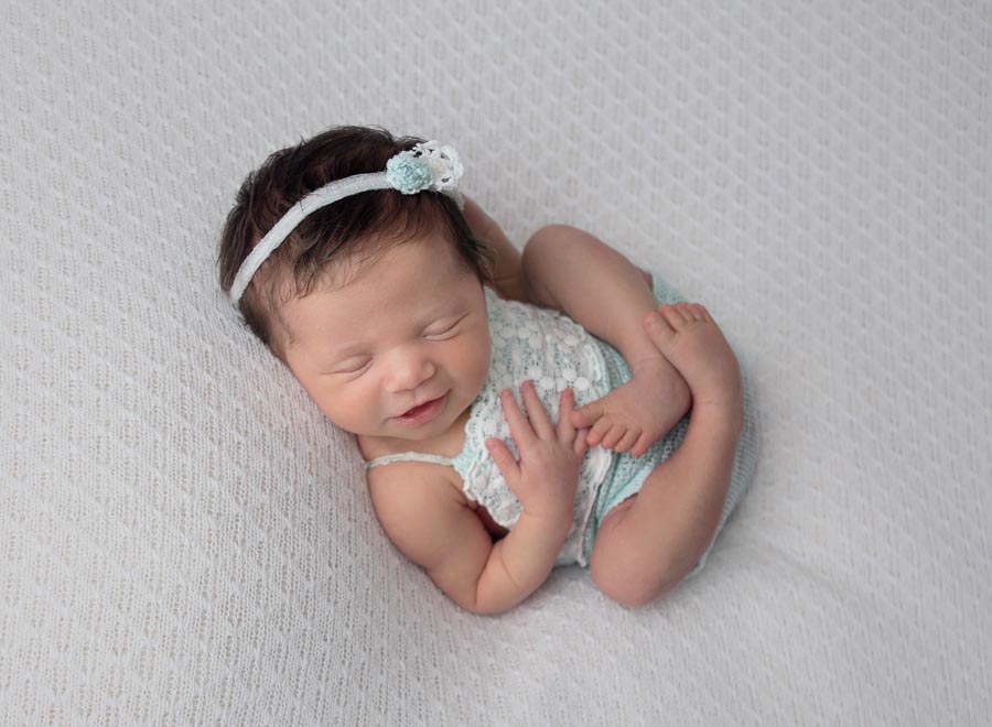 10 day old newborn baby girl in a mint green outfit and headband posed on a cream backdrop