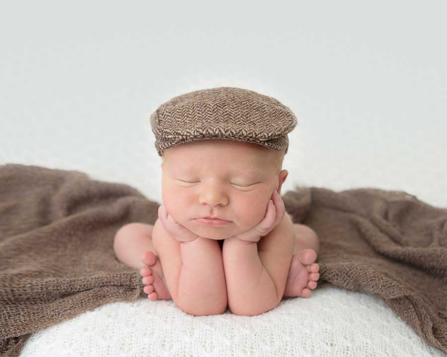 Newborn baby boy wear a with a Yorkshire cap posed in the frog pose on a brown wrap on a cream backdrop in a studio in Doncaster