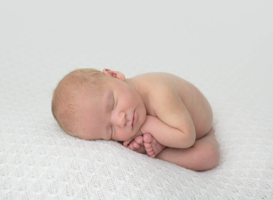 Kaydee's 10 day old baby boy posed in the taco pose wrapped in a blue wrap on a cream backdrop in a photography studio