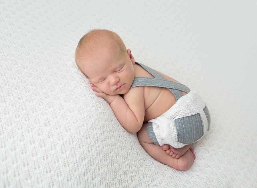 Kaydee's Newborn baby boy posed in the tushy up wearing a cream shorts with grey pocket and suspenders on a cream backdrop in a photography studio in Doncaster