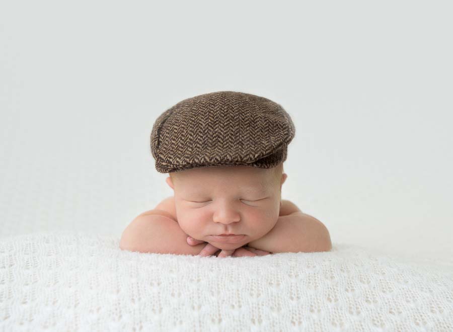 Newborn baby boy posed on his tummy wearing a Yorkshire cap on a cream backdrop in photography studio in Doncaster